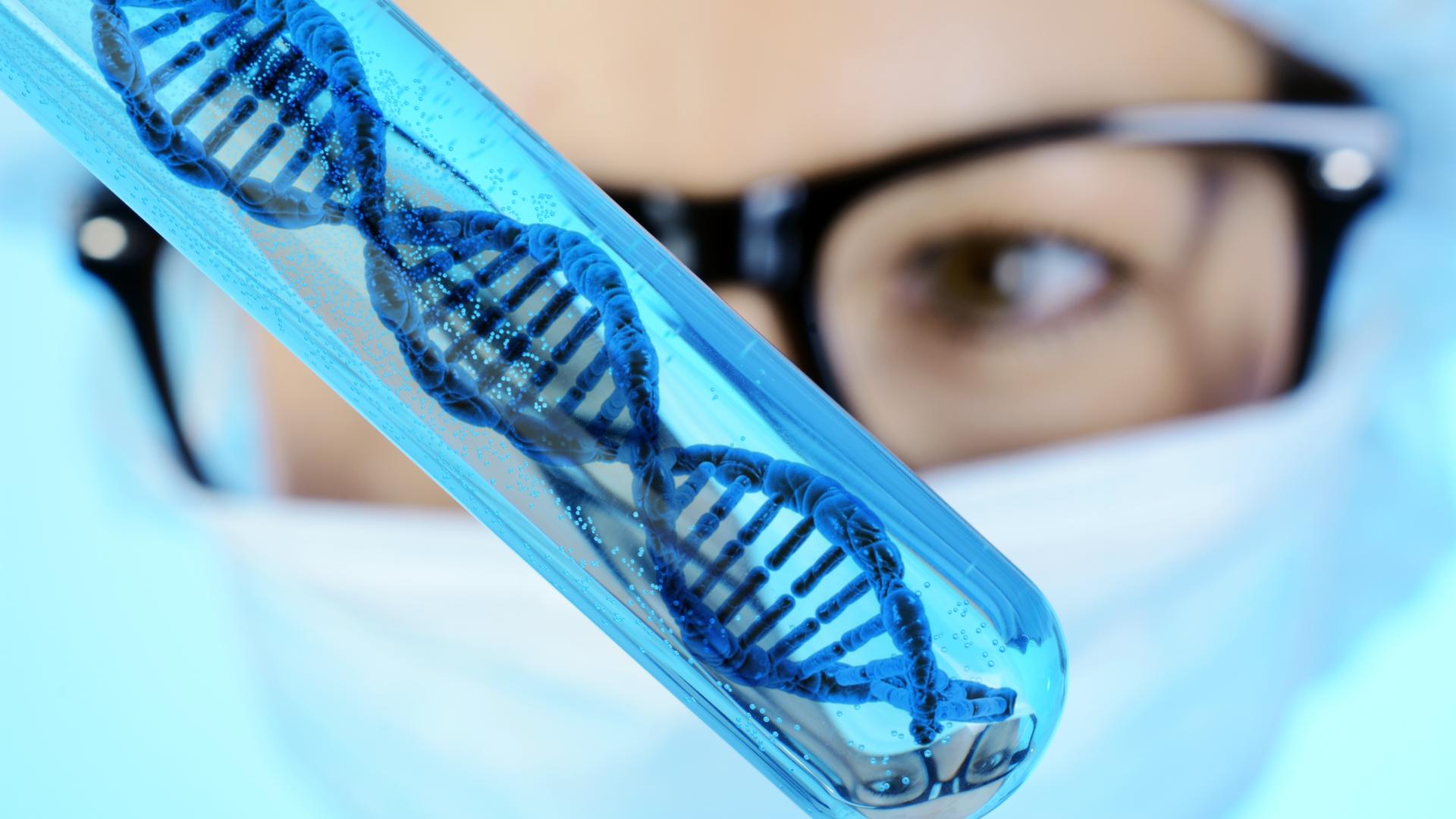 Glasröhrchen mit grafischer DNA-Doppelhelix, im Hintergrund eine Wissenschaftlerin
