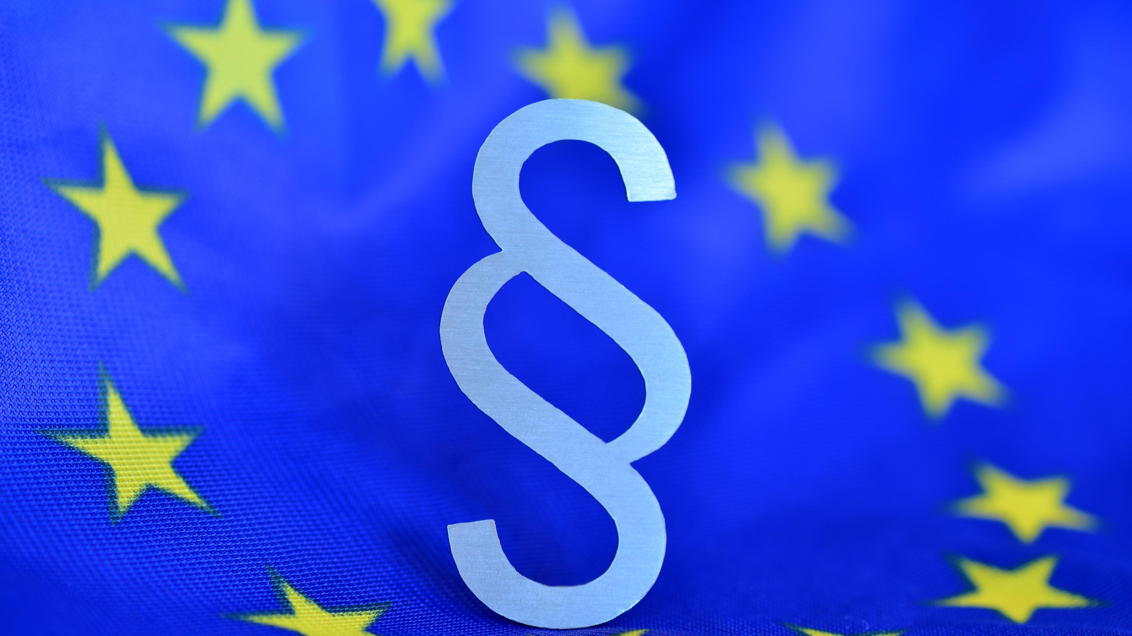 Paragrafenzeichen vor blauer Europaflagge (als Mittelpunkt des Europasternenkreises)