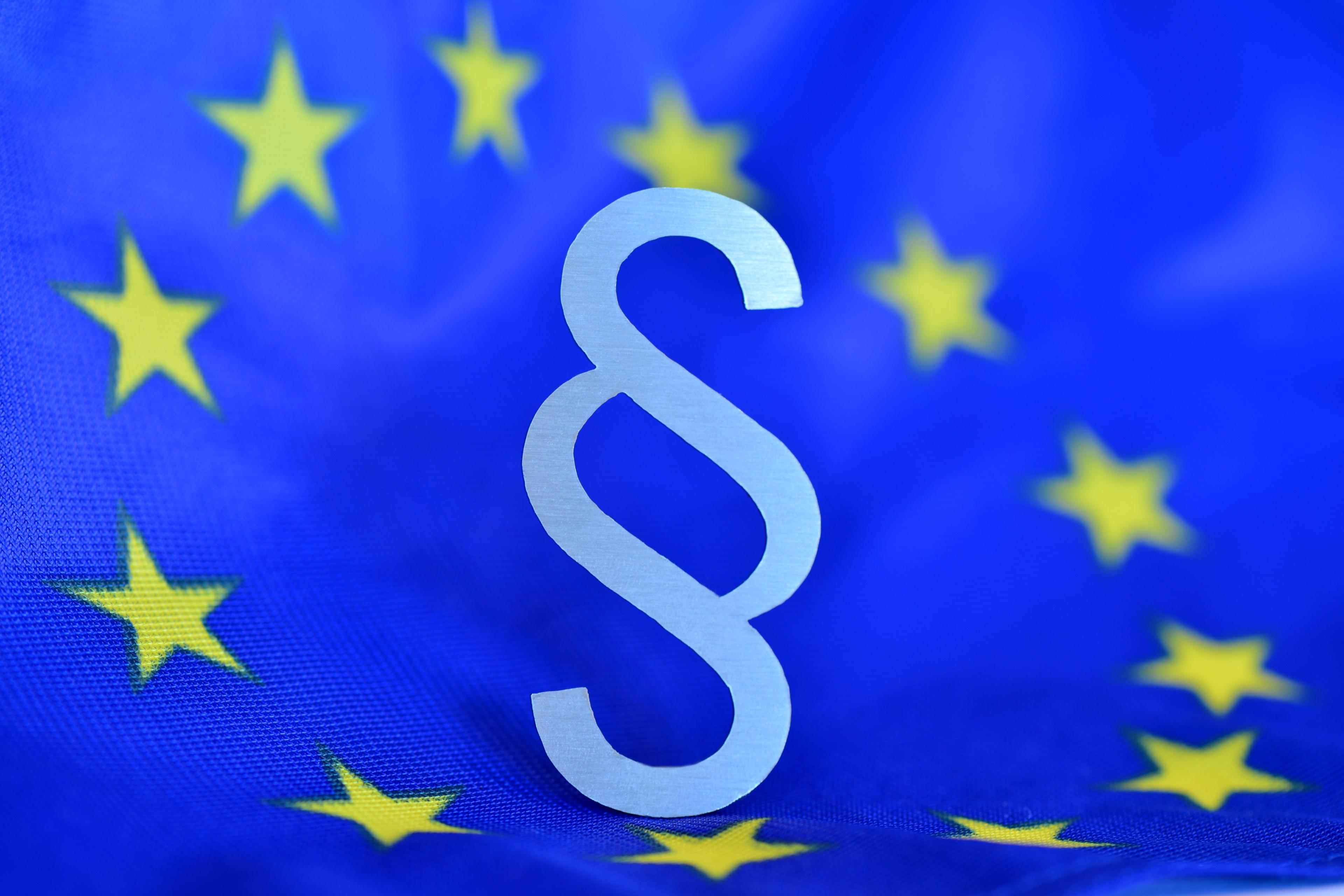 Paragrafenzeichen vor blauer Europaflagge (als Mittelpunkt des Europasternenkreises)
